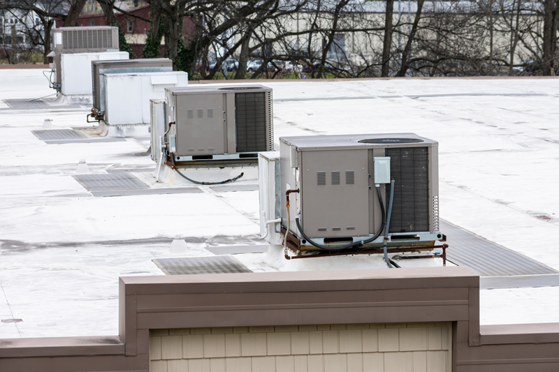 Commercial rooftop air conditioning units lined up on a flat white building roof